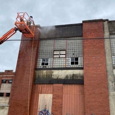 Employee On Lift Actively Pressure Washing Industrial Building in Chattanooga TN by QualityPRO Power Washing