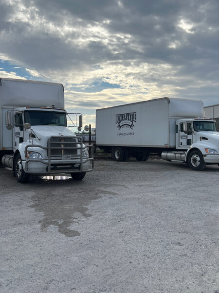 Two white semi trucks parked on a gravel lot under a cloudy sky; a Dunlap & Kyle trailer is visible.