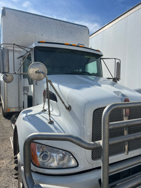 Front view of a white semi-truck with a heavy-duty bumper guard and large side mirrors under a blue sky, parked outdoors.