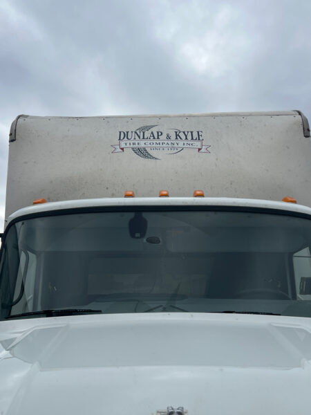 Front view of a white delivery truck with a large box in the background, showing the Dunlap & Kyle Tire Company Inc. logo on the cargo area.