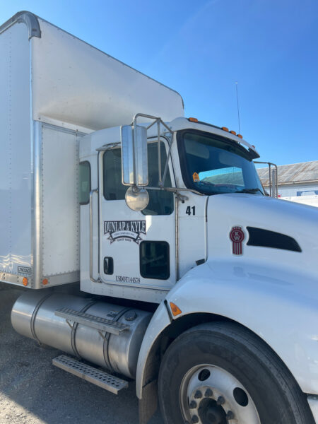 White semi-truck tractor with a tall box trailer, chrome mirrors, and a Dunlap & Kyle logo on the door; truck number 41 visible.