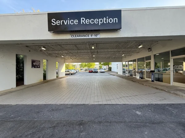 Covered driveway to a service reception area with a large 'Service Reception' sign overhead and cars parked beyond.