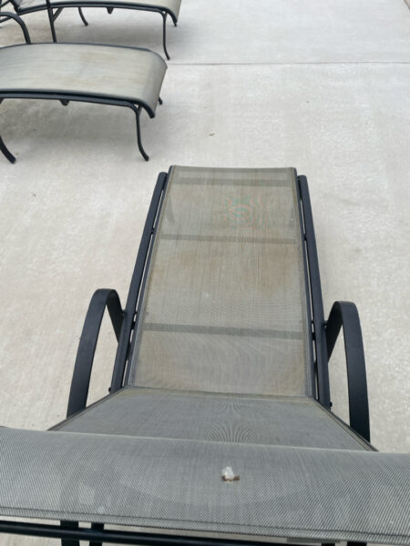 Empty outdoor mesh lounge chair on a concrete patio, with curved metal chairs in the background.