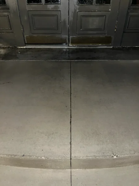 Commercial concrete pressure washing completed at a building entrance, removing heavy dirt and grime buildup to restore a cleaner, brighter, and safer walkway.