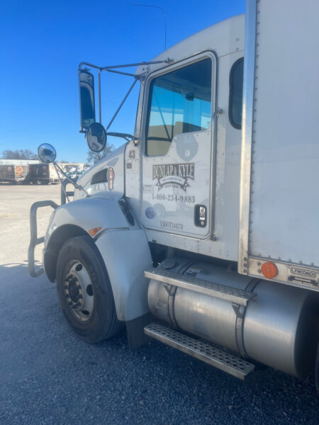 White semi-truck cab in a truck yard, door showing Dunlap & Kyle logo and contact info, with a large chrome fuel tank and steps nearby