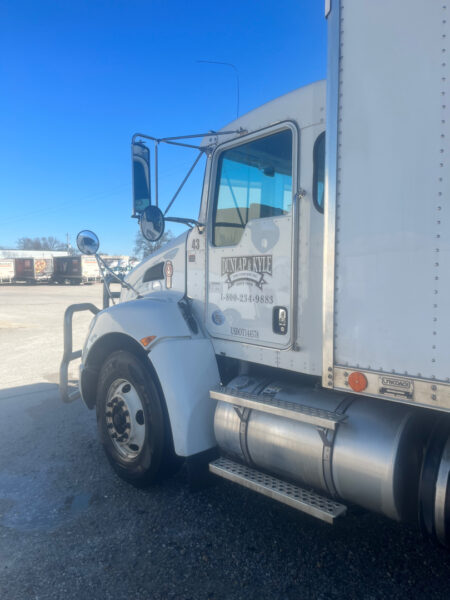 White semi-truck cab with Dunlap & Kyle logo on the door, chrome mirrors, and metal steps, parked in a truck lot under a blue sky.