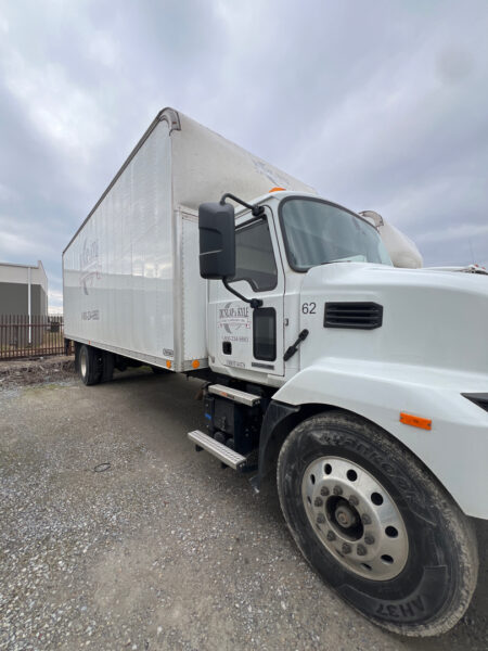White cargo box truck with cab and large side mirror, parked on gravel; door shows company logo and number 62