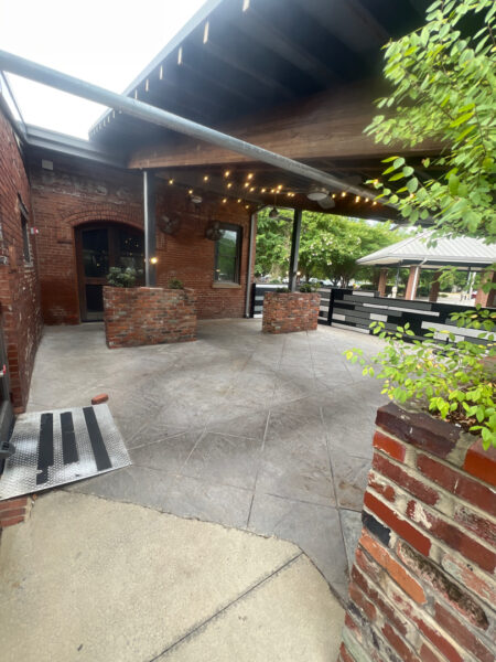 Brick-walled outdoor patio with string lights, planters, and a covered walkway near a brick building.