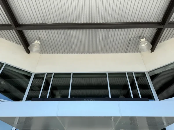 Exterior view of a storefront with large glass windows under a corrugated metal roof and two industrial-style lights above the entrance.