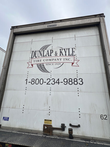 Back of a white truck trailer with Dunlap & Kyle Tire Company logo and the phone number 1-800-234-9883; trailer door panels visible, 62 in lower right corner.