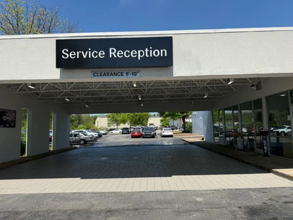 Facade of a car service center with a covered driveway and a large 'Service Reception' sign above the entrance, clearance bar visible underneath