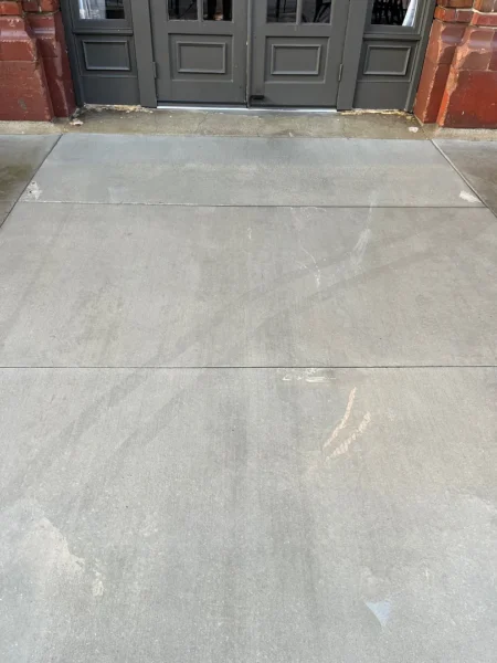 Commercial concrete pressure washing completed at a building entrance, removing heavy dirt and grime buildup to restore a cleaner, brighter, and safer walkway.