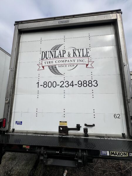 Rear of a white semi-trailer with Dunlap & Kyle Tire Company logo and phone number, 1-800-234-9883, on the door panel