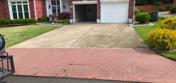 Two-car brick house with an open garage door, concrete driveway, and a brick-paver foreground leading to the street, with trimmed lawn and shrubs on both sides.