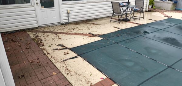 Backyard scene with a covered pool, nearby patio table and chairs, and leaves scattered on the ground.