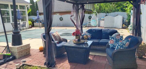 Cozy outdoor seating area under a gazebo with navy wicker sofa set and floral cushions on a brick patio.** Note: remove the asterisks**