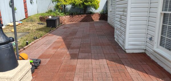 Red brick-paver patio running along the house, with a brick raised planter at the far end and an outdoor AC unit on the left.