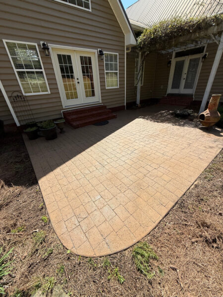 Curved brick-paver patio in front of a house with double doors and multiple entryways, potted plants on the left, and a clay chiminea on the right.