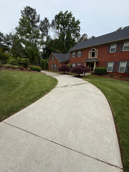 Curved concrete sidewalk through a suburban lawn toward red brick townhouses with trimmed shrubs and trees.