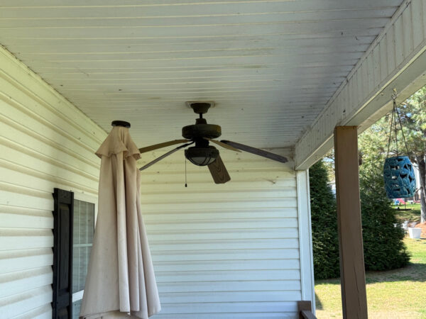 Back porch with a ceiling fan, a folded beige patio umbrella leaning against the wall, and a blue patterned hanging lantern by a support post.