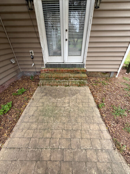 Concrete paver path leading to brick steps up to white double doors with blinds, beige siding, and mulch beds on both sides of the walkway.