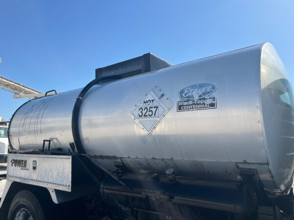 Shiny silver tanker trailer on a truck, with a hazardous materials placard reading 3257 and a 'Etire Black-Topp Centennial' sticker visible on the side.