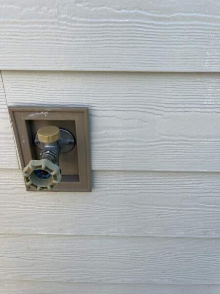 Outdoor hose bib with beige knob on a siding wall plate, ready to turn water on/off.
