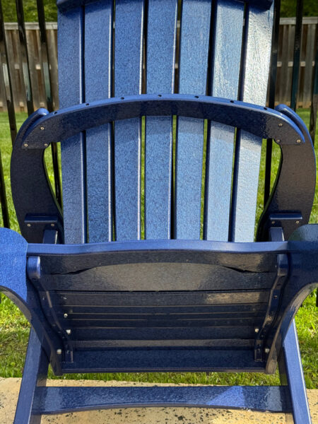 Close-up of a blue outdoor Adirondack chair with a curved backrest and armrests, placed on a patio.
