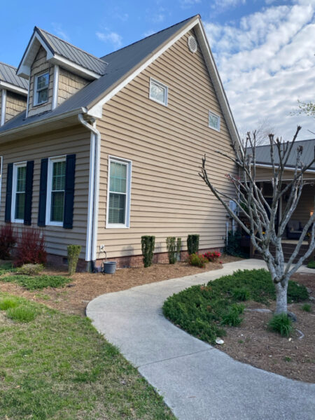 Two-story beige house with blue shutters and a curved concrete walkway in the front yard.
