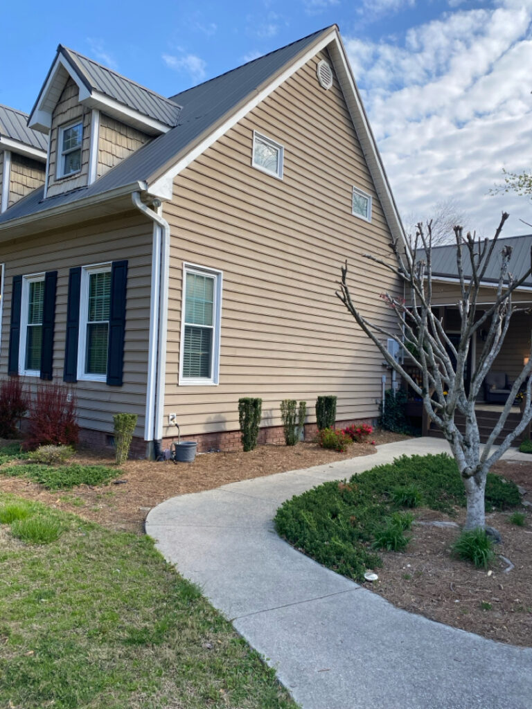 Two-story beige house with blue shutters and a curved concrete walkway in the front yard.