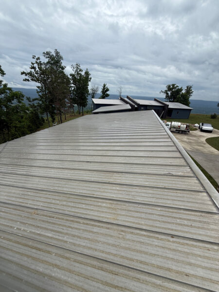 Aerial view from a silver metal roof looking toward trees and a hillside campus with grey buildings under a cloudy sky.