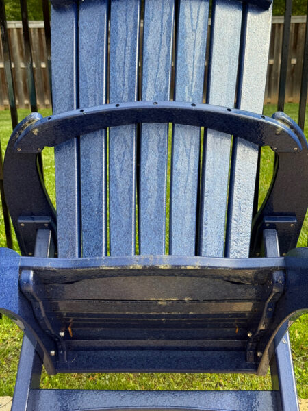 Blue outdoor Adirondack chair close-up, showing worn paint and curved armrest details on a grassy lawn.