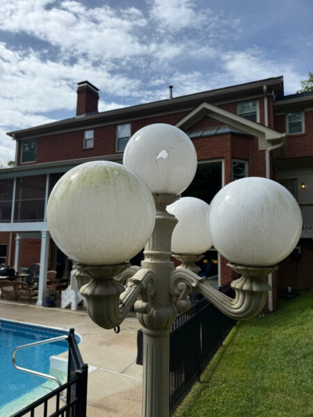 Decorative four-globe street lamp by a poolside courtyard with a brick building in the background.