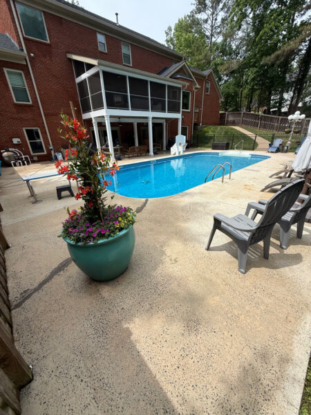 Backyard pool area of a brick house with a blue rectangular pool, screened porch, and plastic lounge chairs nearby.
