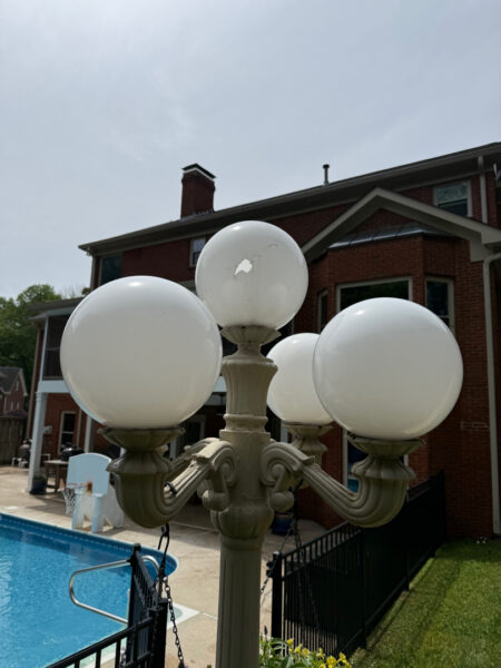 Ornate four-globe lamp post beside a swimming pool, with a brick building in the background.