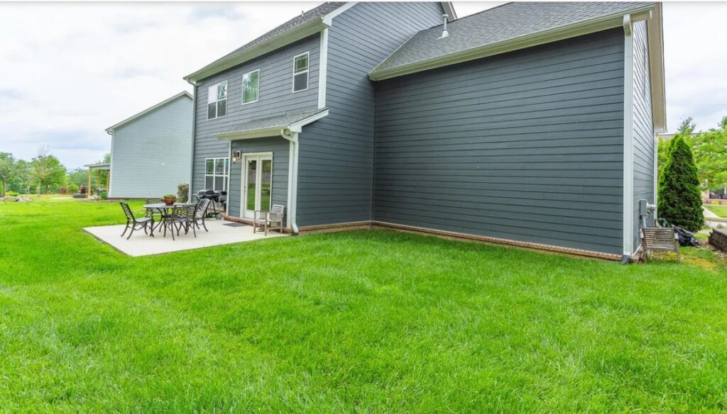 Backyard of a two-story blue house with a concrete patio table and chairs