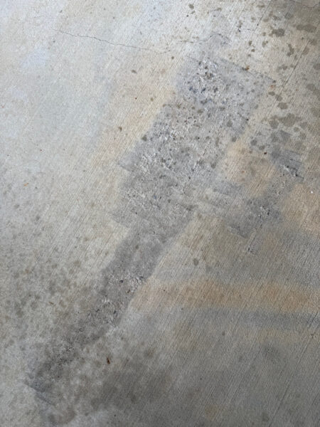 Concrete floor with a diagonal wet or stained streak and small dark spots across the surface.