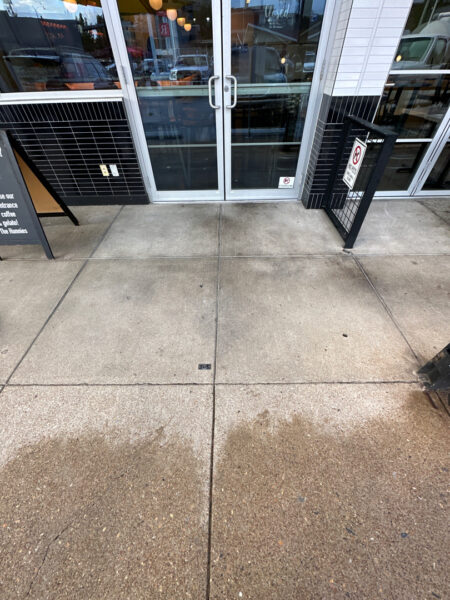 The front patio concrete at Milk and Honey was professionally restored through a multi-step process involving site protection, specialized detergent application, targeted pressure washing, and a final rinse to remove organic growth and grease.