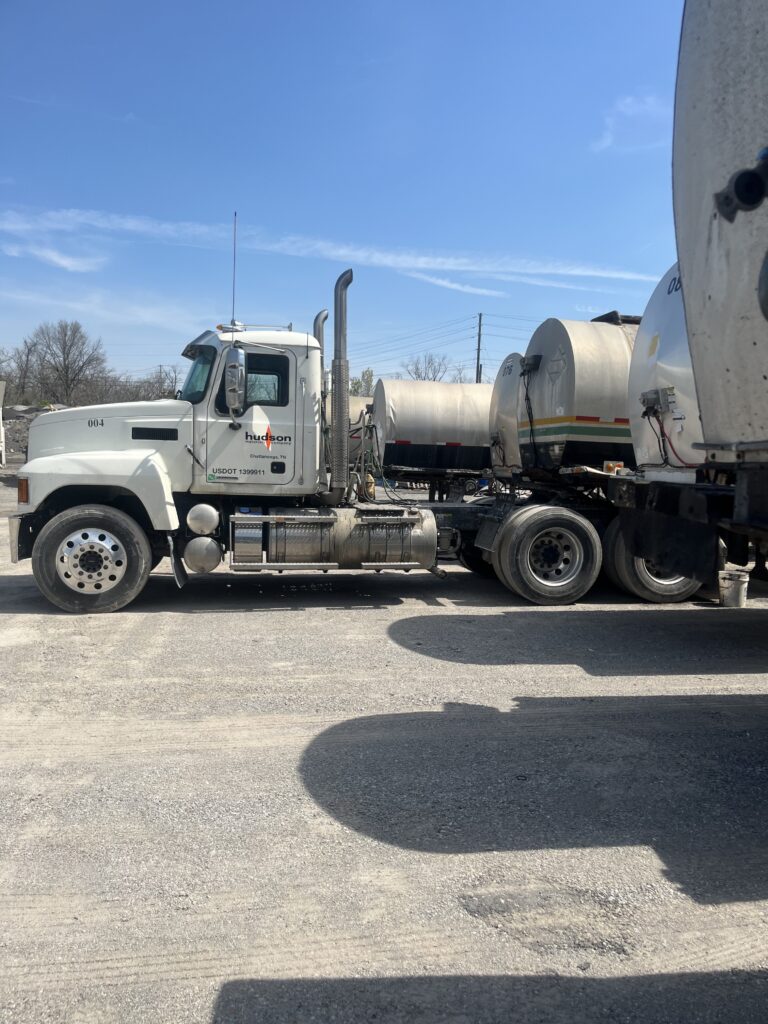 White semi-truck with a fuel tanker trailer at a truck yard under a clear blue sky.