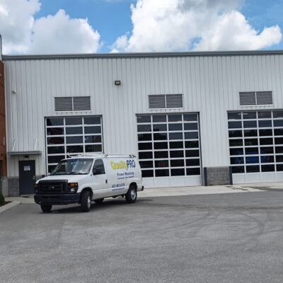 White service van labeled 'QualityPRO Power Washing' parked in front of a large industrial building with multiple garage bays under a cloudy sky.