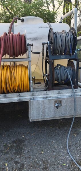 Hoses coiled on reels mounted on a service truck, with a large white tank behind and a diamond-plate storage box below.
