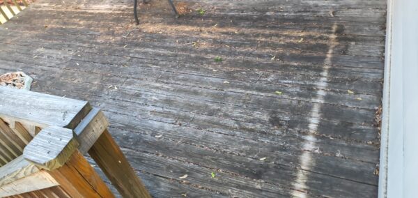 Weathered wooden deck with scattered leaves and a railing visible on the left side.