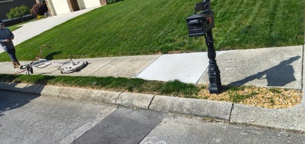 Man standing on a residential sidewalk near a driveway, with a large floor buffer resting on the path.