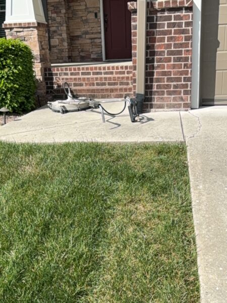 Front porch of a brick house with a dark red door; a broken metal frame sits on the concrete sidewalk near the steps.