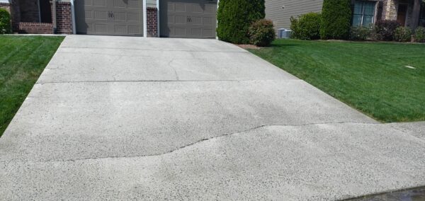 Cracked concrete driveway leading to a two-car garage, with well-kept green lawns on either side of the driveway.