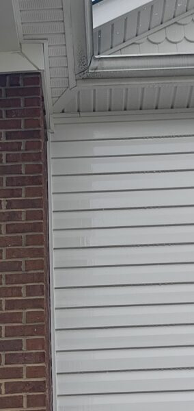 Close-up of a house corner showing a brick wall on the left and white horizontal siding with a gutter and soffit above.