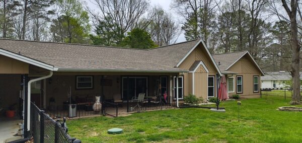 Backyard of a single-story beige house with a covered patio, outdoor seating, and a black metal fence.