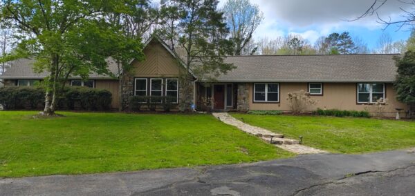 Front view of a single-story ranch house with stone front, tan siding, and a curved stone walkway to the red front door on a green lawn.