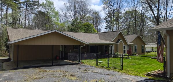 Single-story suburban home with a large carport, fenced yard, and an American flag near the front lawn.