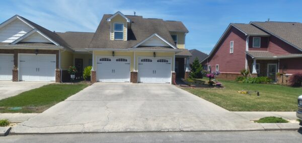 Three houses in a suburban street with attached garages; yellow-center home, white left garage, red house on the right under a blue sky with green lawns.